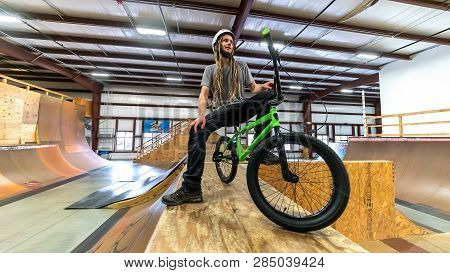 Portrait Of A Man With Dredlocks And A Helmet On A Bmx Bike At An Extreme Sports Park
