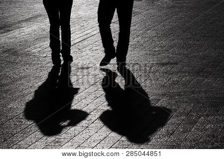 Couple Walking Down The Street, Silhouettes And Shadows Of Two People On Pedestrian Sidewalk. Male A
