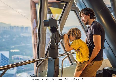 Dad And Son Are Looking At Kuala Lumpur Cityscape. Use Binoculars. Panoramic View Of Kuala Lumpur Ci