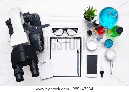 Laboratory Table With A Blank Paper Sheet Of Researching Results, Microscope, Mobile Phone And A Che