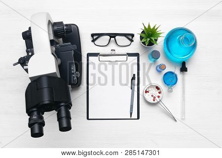 Laboratory Table With A Blank Paper Sheet Of Researching Results, Microscope And A Chemical Reagent 