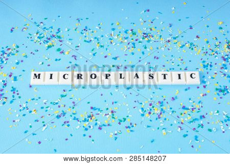 Word Microplastic Around Small Plastic Particles On A Blue Background. Microplastic In Water And Foo