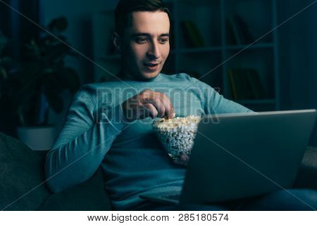 Handsome Man Watching Movie On Laptop And Holding Bowl With Popcorn At Home