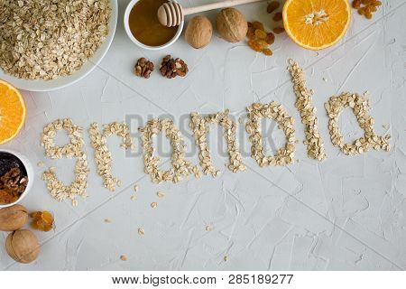 Ingredients For Granola. The Word Granola Made From Oat Flakes On A Grey Background