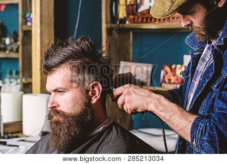 Hipster Client Getting Haircut. Barber With Hair Clipper Works On Hairstyle For Man With Beard, Barb