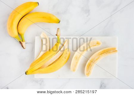 Bananas And Banana Halves On White Marble Chopping Board And Marble Background. Top View.