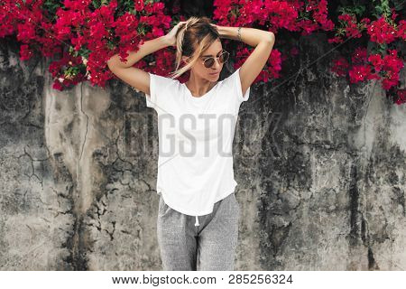 Hipster girl wearing blank white t-shirt posing against gray street wall with spring flowers, blank mockup for tshirt print store