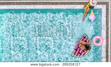 Two people (mom and child) relaxing on watermelon lilo in the pool at private villa. Summer holiday idyllic. High view from above.