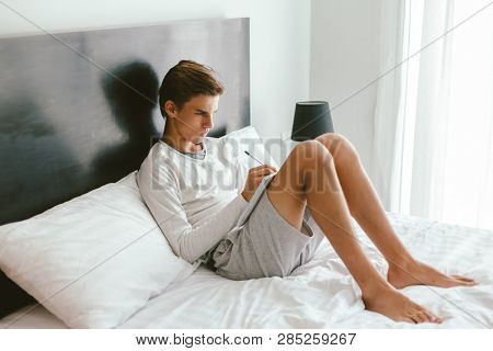 16 years old teenage boy prepare for exams while relaxing on couch in his room