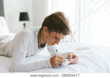 16 years old teenage boy writing school notes or doing homework while relaxing on couch in his room