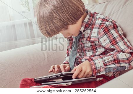 Young Caucasian Schoolboy Wearing A Checkered Shirt With Tie Using A Digital Tablet Sitting On A Cou