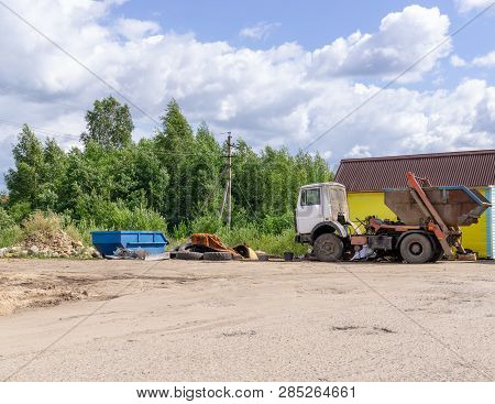 Dustcart With Bin Lift, Empty Garbage Container, Waste Dump Are On Sandy Area Next To Trees. Copy Sp