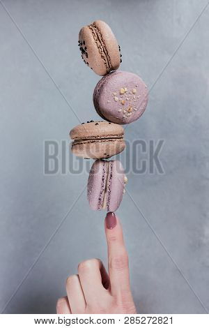 Sweet French Macaroons Cookies Stacked On Woman's Finger Against Grey Background