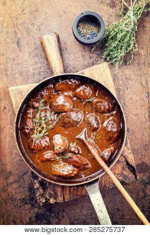 Traditional German braised pork cheeks in brown red wine sauce with mushroom and onions as top view in a casserole 