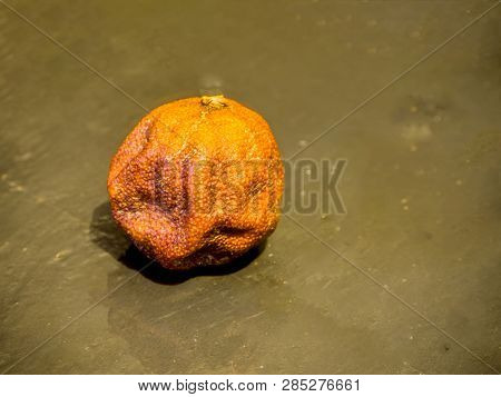 The Old Wrinkled Stale Overripe Mandarin.  Rotten Black Stone Dish Background. Top View. Free Copy S
