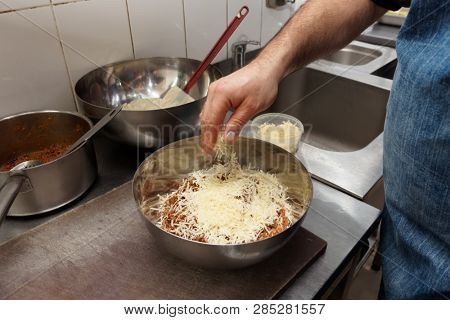 Chef is springling some grated cheese on ground meat with bechamel, making moussaka stuffing