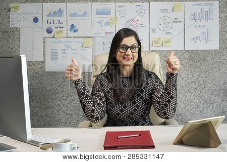 Portrait Of Happy Mature Bsuiness Lady Sitting At Her Office Desk And Showing Thumbs-up