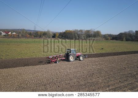 A Farmer On A Red Tractor With A Seeder Sows Grain In Plowed Land In A Private Field In The Village 
