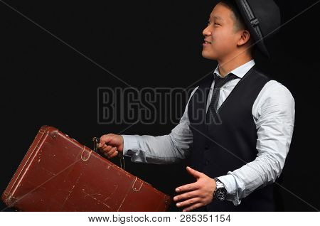 Asian Young Man Wearing A Hat With A Suitcase, Smiling And Lifting His Arms Looking Sideways