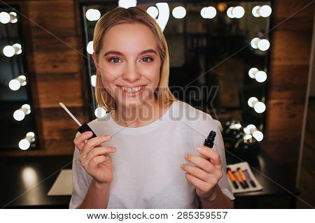 Cheerful Positive Young Woman Look On Camera And Smile. She Hold Lipgloss And Pose. Mirror With Ligh