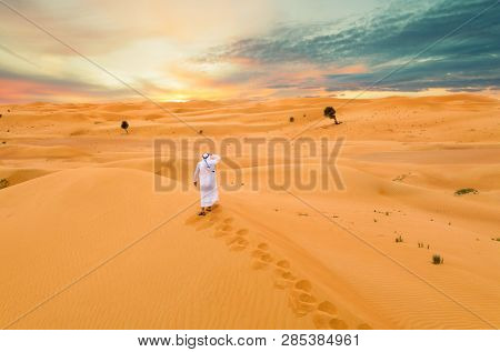 Arabic man with traditional emirates clothes in the desert, sunset.