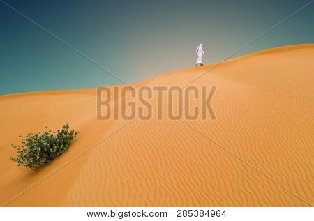 Arabic man with traditional emirates clothes in the desert, sunset.