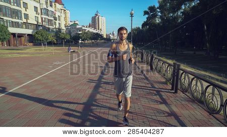 Young Sport Athletic Guy In Shorts And A T-shirt Runs Ahead On A Path Near The House. Boy Sets The C