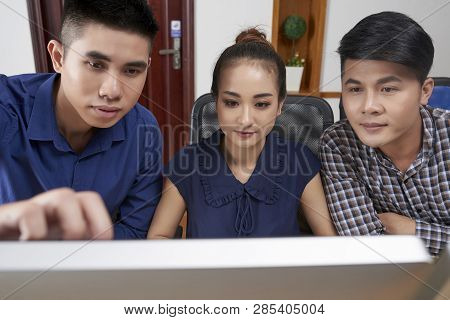 Young Team Of Startuppers Gathered At Computer Monitor And Discussing Report