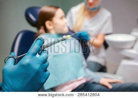 Cut View Of Hand In Latex Glove Holding Dental Tool. Female Dentist Stand Beside Girl In Room. Child