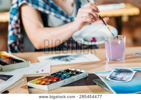 Watercolor Painting. Artist At Work. Painter Dunking Brush In Water. Skethes And Palette Supplies Ar