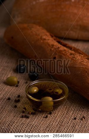 Fresh Bread Baguette With Olive Oil, Olives. Cheese And Rosemary On Wooden Background. Teasty Breakf