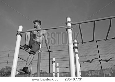 Sportsman With Bare Torso On Monkey Bars Top. Man Athlete Climb On Metal Jungle Gym On Blue Sky. Mac