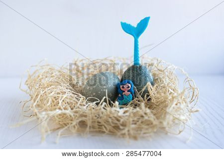 Easter Eggs Lie In A Nest On A White Wooden Background. Two Blue Eggs. Little Mermaid Sitting In The