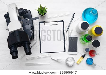 Laboratory Table With A Blank Paper Sheet Of Researching Results, Microscope, Mobile Phone And A Che