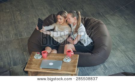 Two Women Take A  Photo  Yourselves With Digital Tablet In Cafe. Sitting On The Sofa Eating Desserts