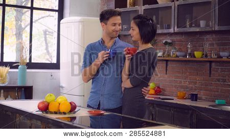 Happy Couple Drinking Coffee Or Tea On The Kitchen At Home. Loft Room With Big Windows. Family Talks