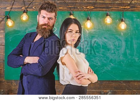 Man With Beard And Teacher In Eyeglasses Stand Back To Back, Chalkboard On Background. Teacher And S
