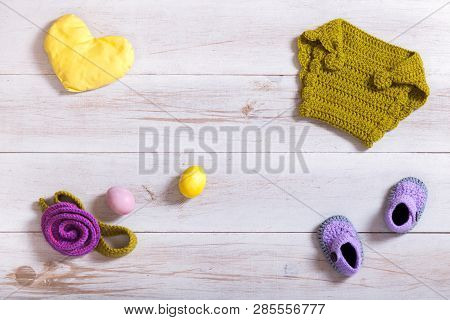 Knitted Baby Clothes And Accessories On White Wooden Background, Newborn Handmade Clothing Set, Kid