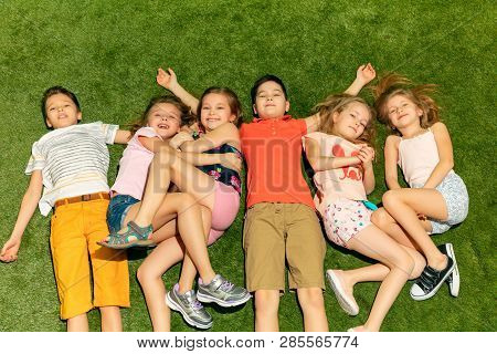 Group Of Happy Children Playing Outdoors. Kids Having Fun In Spring Park. Friends Lying On Green Gra