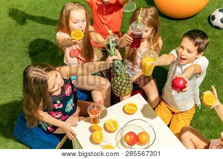 Kids Fashion Concept. The Group Of Teen Boys And Girls Sitting On Green Grass At Park. Children Colo