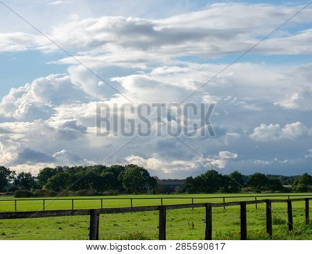 Peasantry With Lush Meadows, Trees, Fence And Blue Cloud Sky At Dusk. Location: Germany, North Rhine