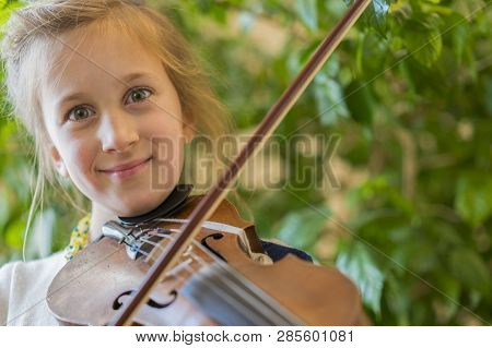 Close Up Of A Child Playing Violin On Green Background. Portrait Of Girl With String And Playing Vio