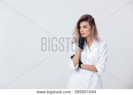 Portrait Of Young Female Professional Cosmetologist In Black Gloves Thinking. Woman Beautician Docto