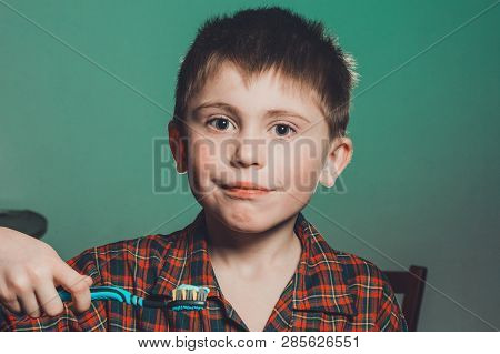 A Beautiful Little Boy In A Pajamas Smiles And Holds In His Hand A Toothbrush On A Greenbackground