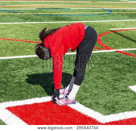 A Teenage Girl Track And Field Runner Is Stretching Her Hamstrings During Winter Outdoor Practice We