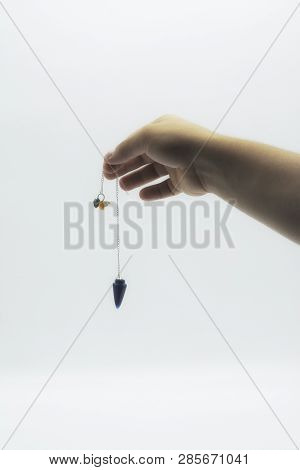 Pendulum Dowsing On An Isolated White Background With An Blue Crystal And Colored Chakra Stones.