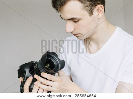 A Young Man Holds A Photo Camera In His Hand And Looks At The Lens In The Dust, A Dirty Lens. Isolat
