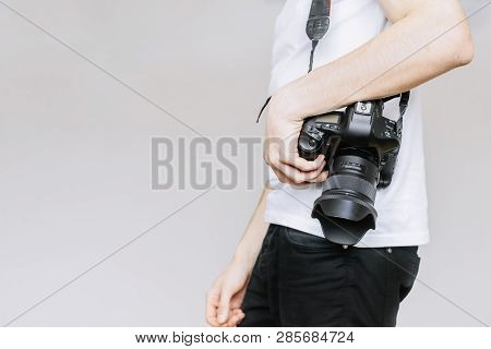 Young Man Carries A Photo Camera On His Shoulder. Isolated Gray Background