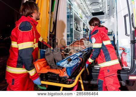 Paramedics Transportating Patient On Gurney In Ambulance Car