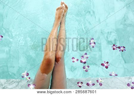 Girl relaxing in tropical spa pool decorated with flowers in luxury hotel, top view photo of female slim legs closeup.